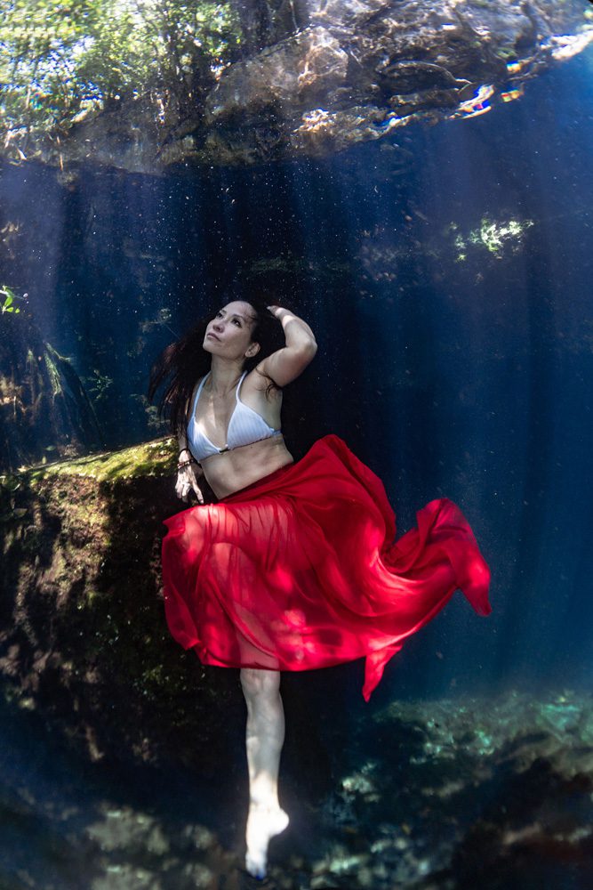 beautiful asian girl posing sitting on a rock underwater, wearing a red skirt, in a cenote in mexico