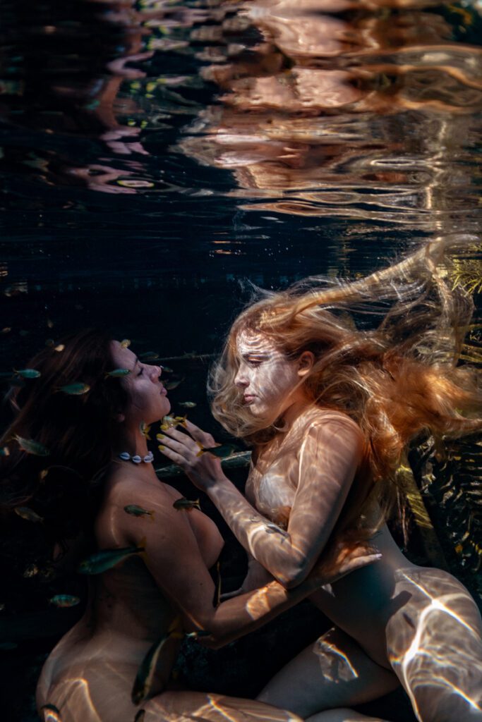 underwater portrait of two women looking at each other and touching their faces