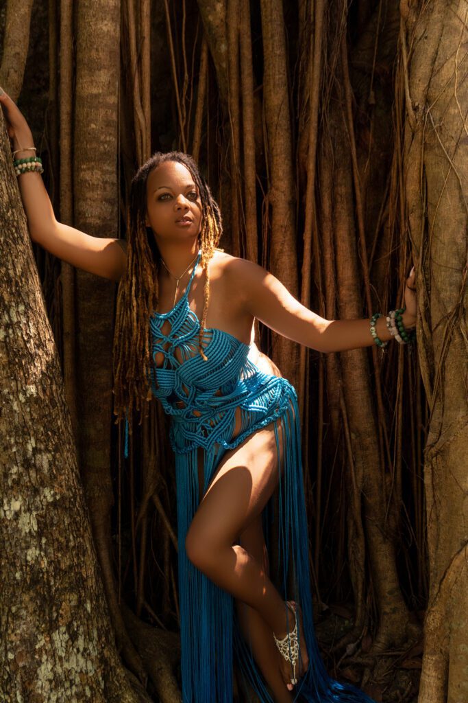 black beautiful girl posing in a tree with vines in a light blue macramé dress