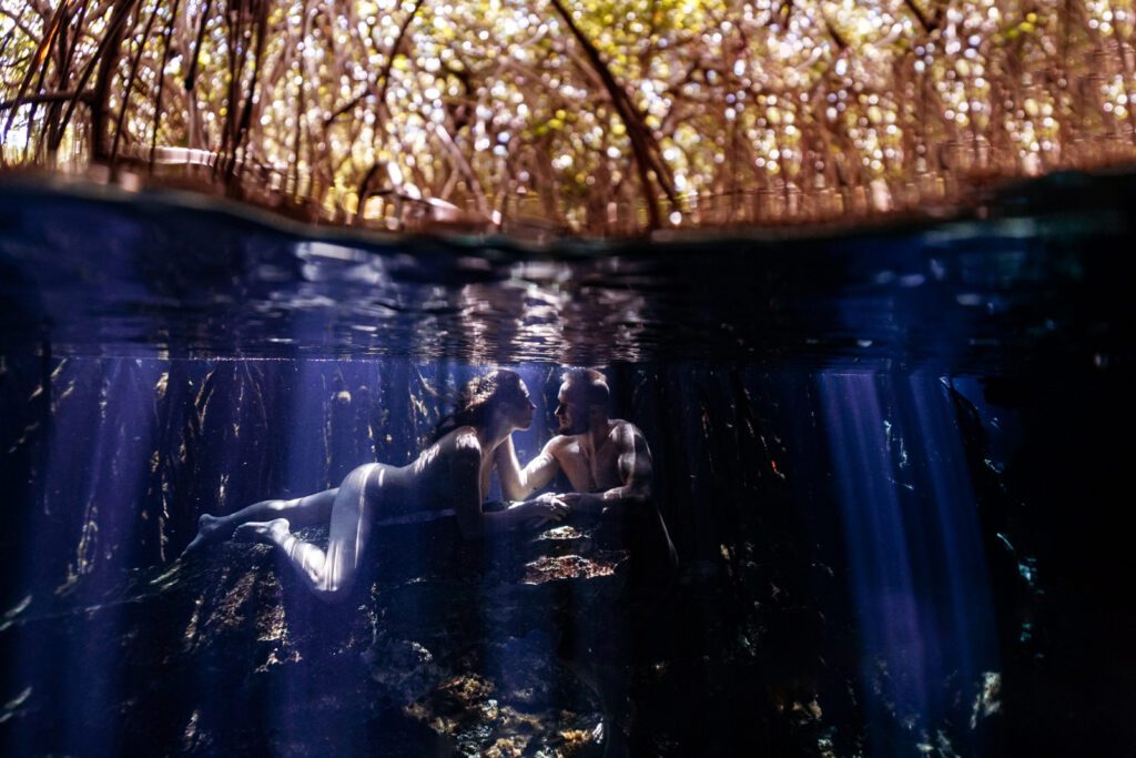 a couple posing underwater in a cenote with incredible rays of light penetrating the water in playa del carmen